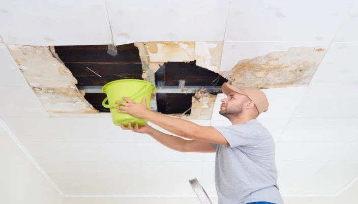 Man catching water from ceiling leak during ceiling & wall leak investigation in Santa Barbara home.